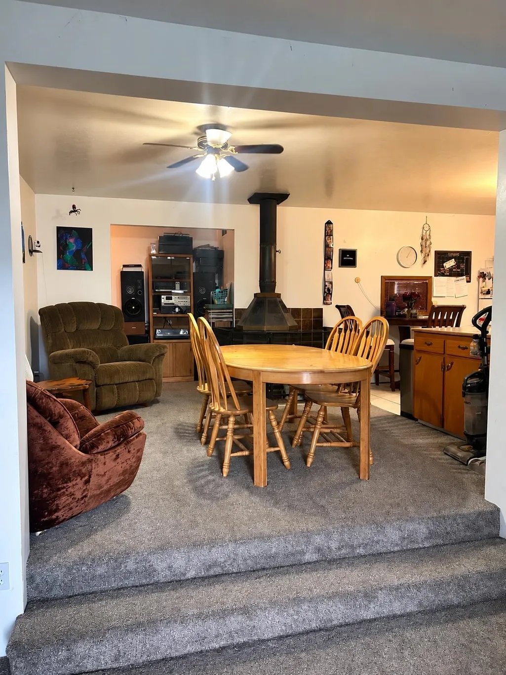 Spacious finished lower-level room with wood dining table, chairs, upholstered recliners, wood stove, and entertainment area with furniture and decor