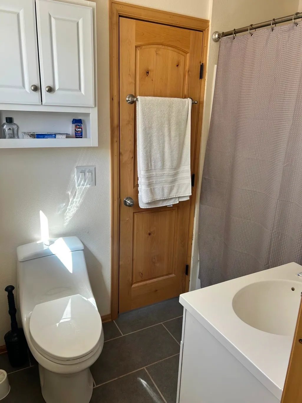Modern bathroom interior with white toilet, wooden door with towel rack, white vanity sink, and shower curtain
