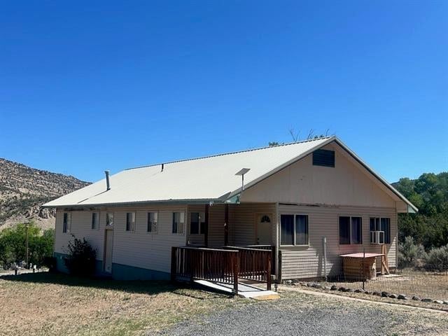 Single-story beige house with covered porch and wooden deck in a desert landscape with dry hills under clear blue sky