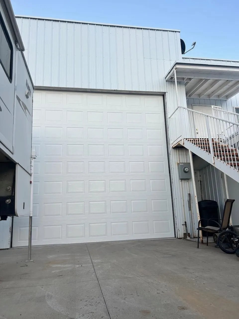 White garage door on metal building exterior with concrete driveway and outdoor items