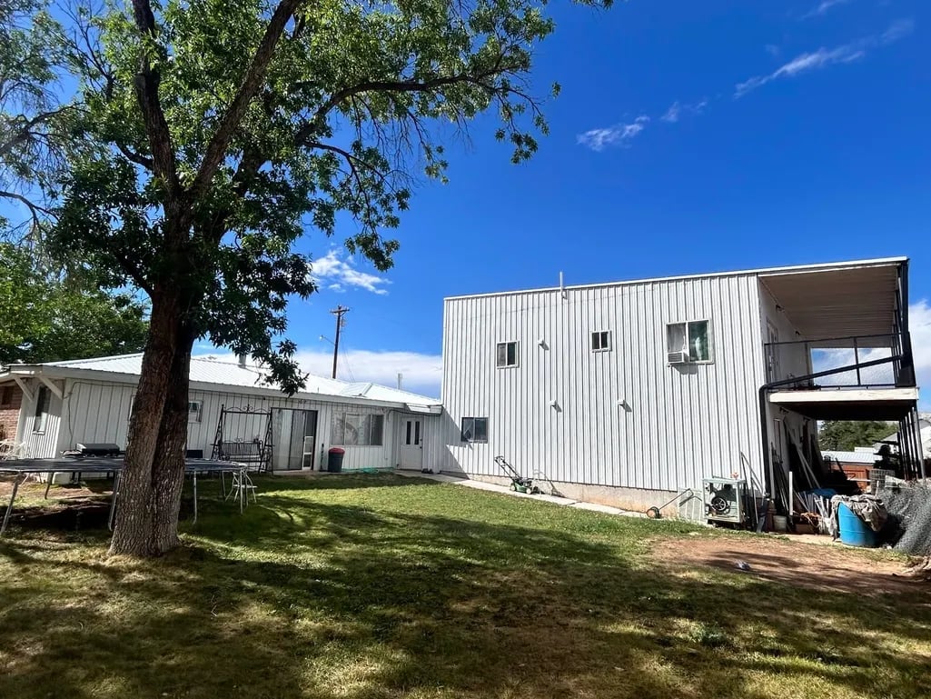 Metal-sided trailer homes on a grassy lot with a large tree, under blue sky
