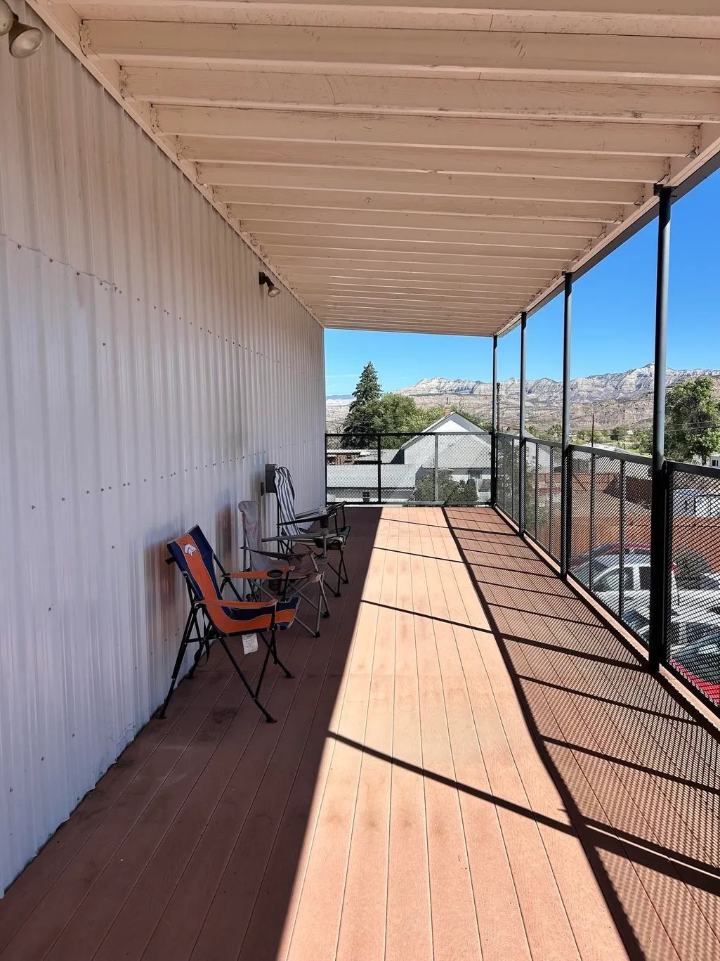Covered deck with wooden flooring, camping chairs, metal railings, and mountain views in the background