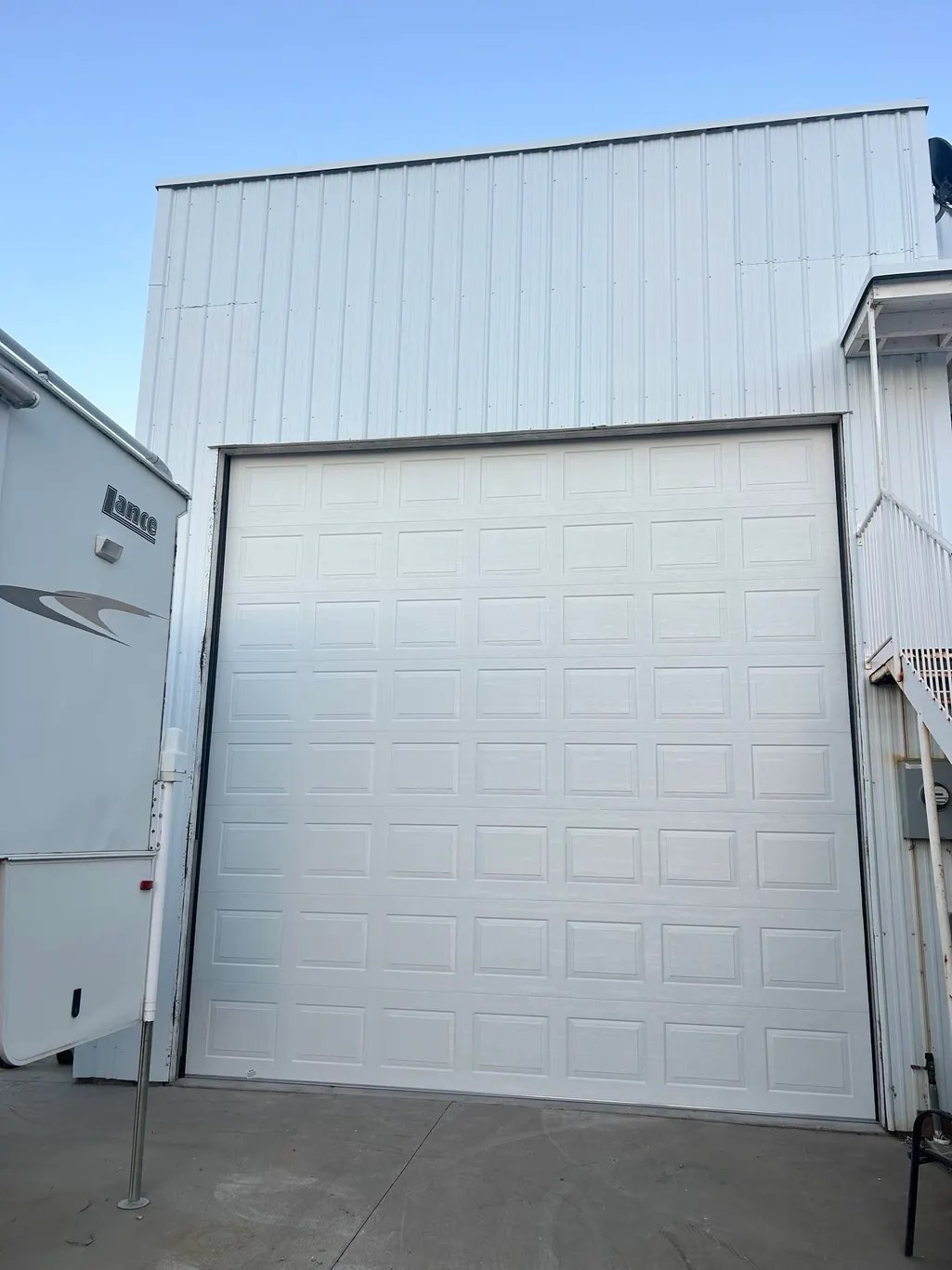 White garage door on industrial metal building with clear blue sky, viewed from driveway
