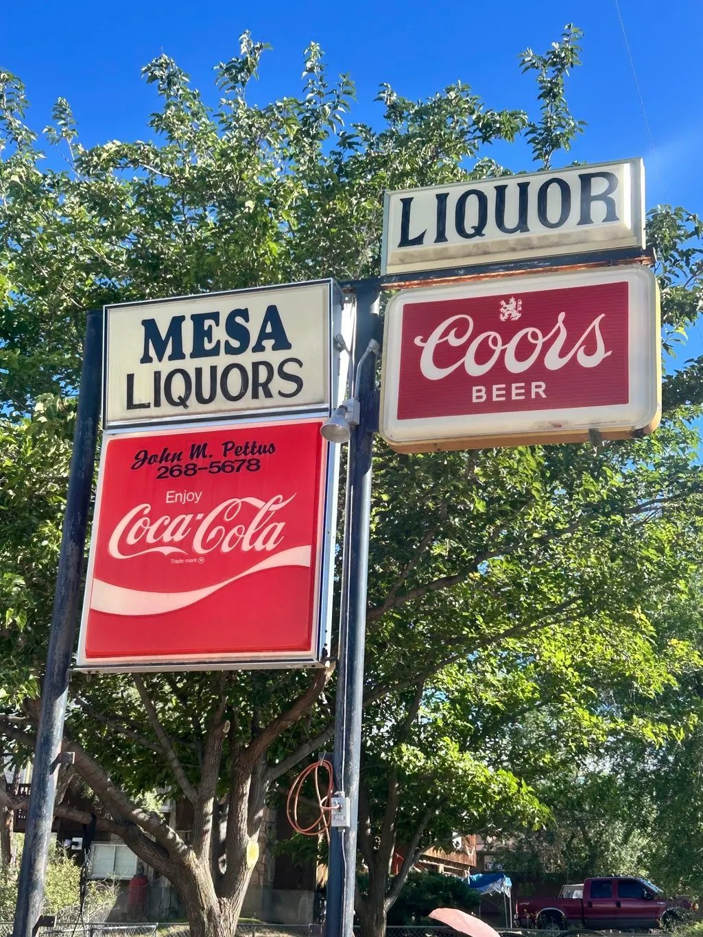 Vintage Mesa Liquors sign with Coors Beer and Coca-Cola advertising panels against blue sky and green trees